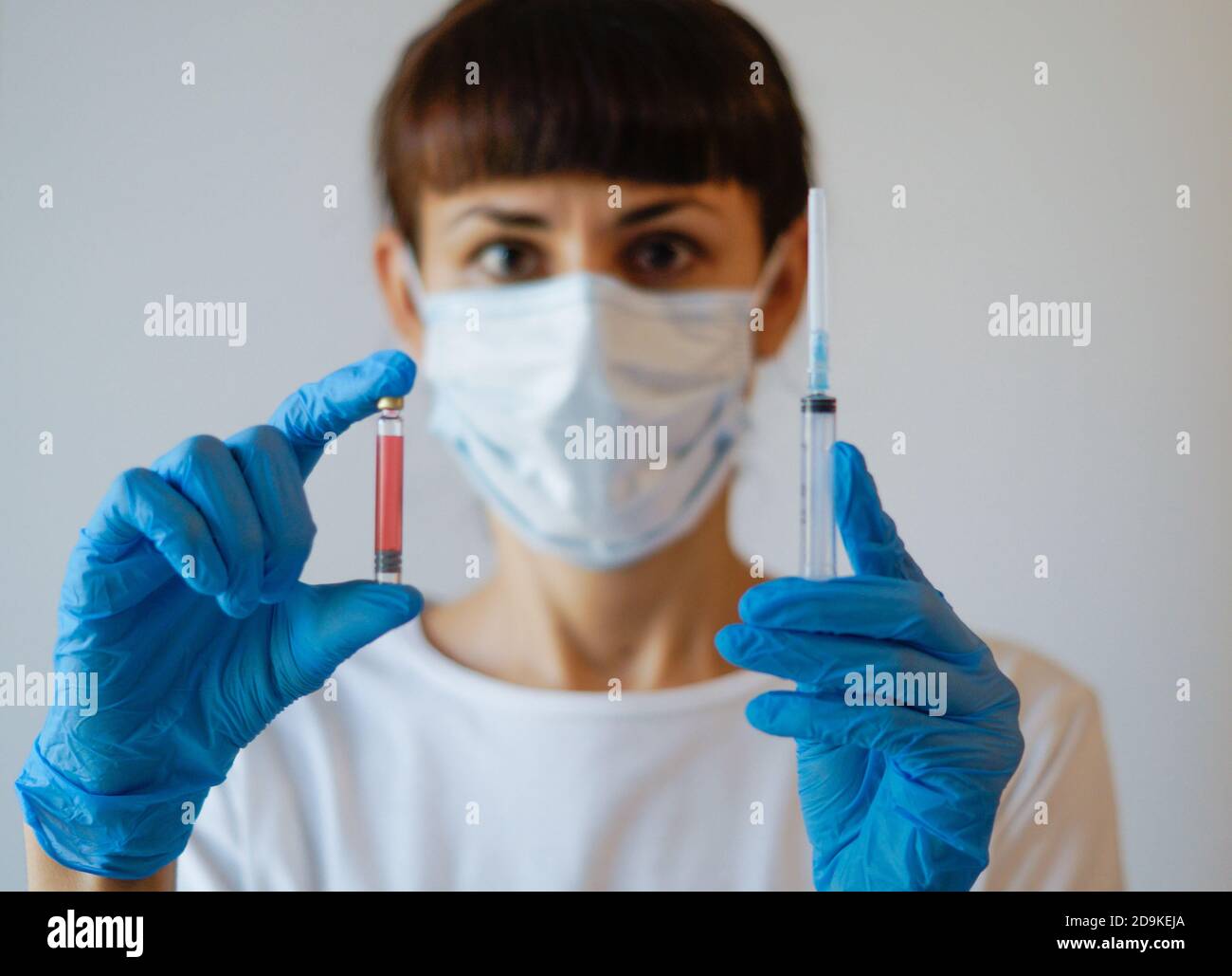 Eine Krankenschwester zieht Gummihandschuhe an und zieht eine medizinische Gesichtsmaske an, eine Ärztin hält eine Spritze und COVID-19-Impfstoff, isolierter weißer Hintergrund, Stockfoto