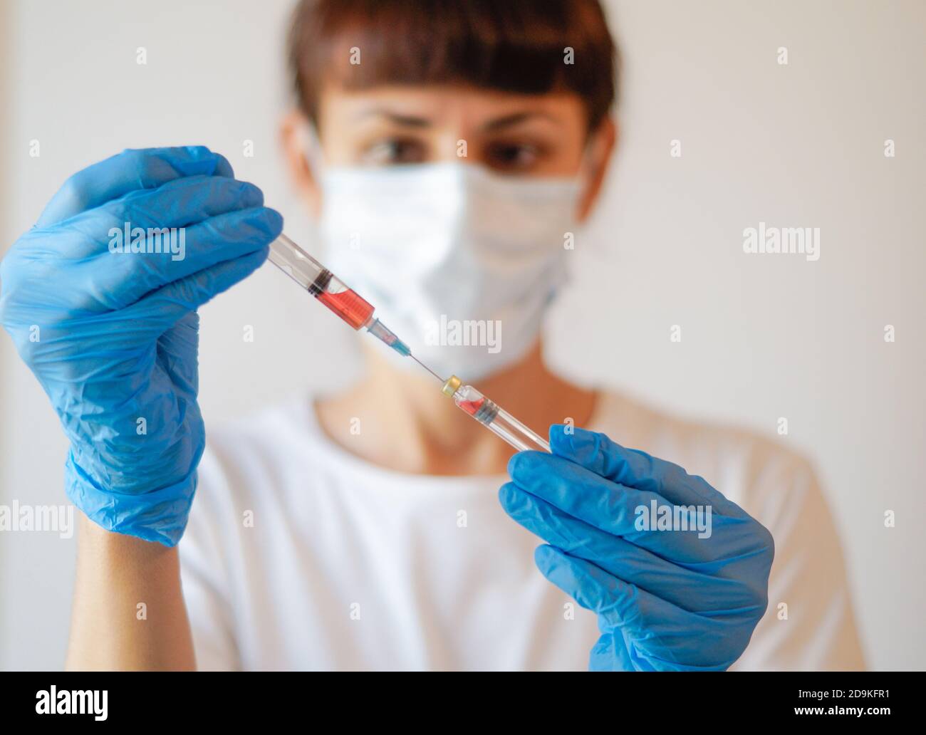 Eine Ärztin oder Krankenschwester in Uniform und Handschuhen und eine schützende Gesichtsmaske im Labor hält eine Nadel, eine Spritze, Medizin und ein Coronavirus vacc Stockfoto