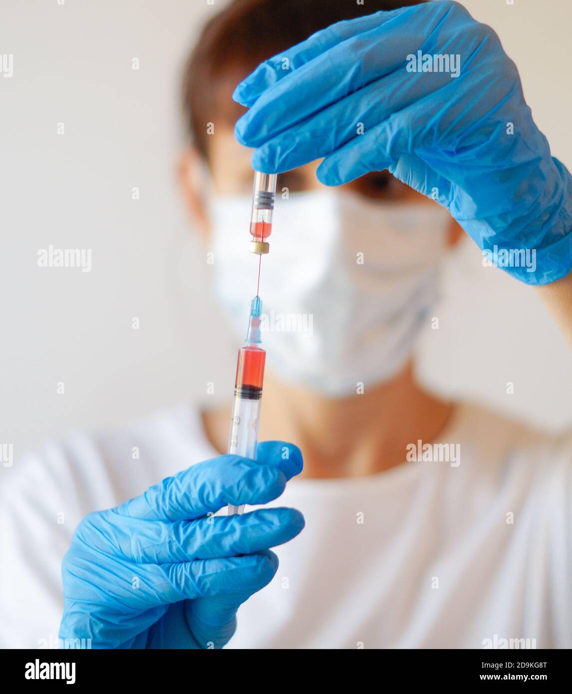 Arzt Krankenschwester Frau trägt Schutzmaske und Handschuhe - hält Virus Blut Teströhrchen und Spritze Stockfoto