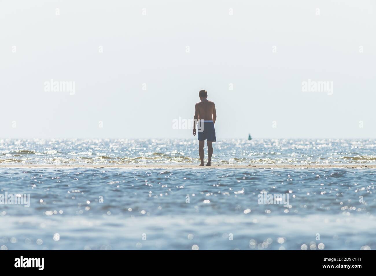 Strandrekreation - Mann in Badehosen blickt über das Wasser und beobachtet die Wellen. Stockfoto