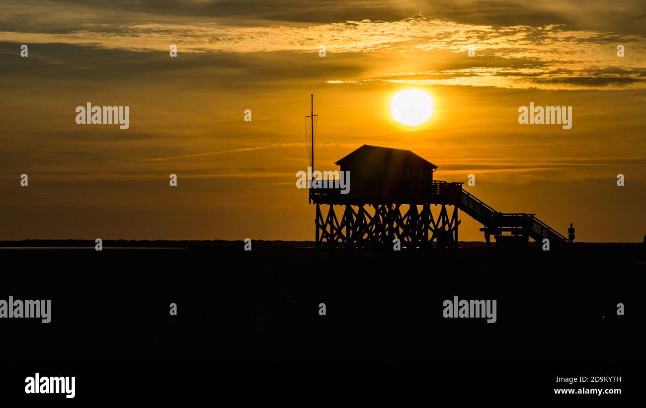 Farbenprächtiger Sonnenuntergang an der Nordsee - im Hintergrund der Sonne ein typisches Stelzenhaus, Pfahlbauten, Pfahlbauten, die den Gezeiten trotzen. Stockfoto