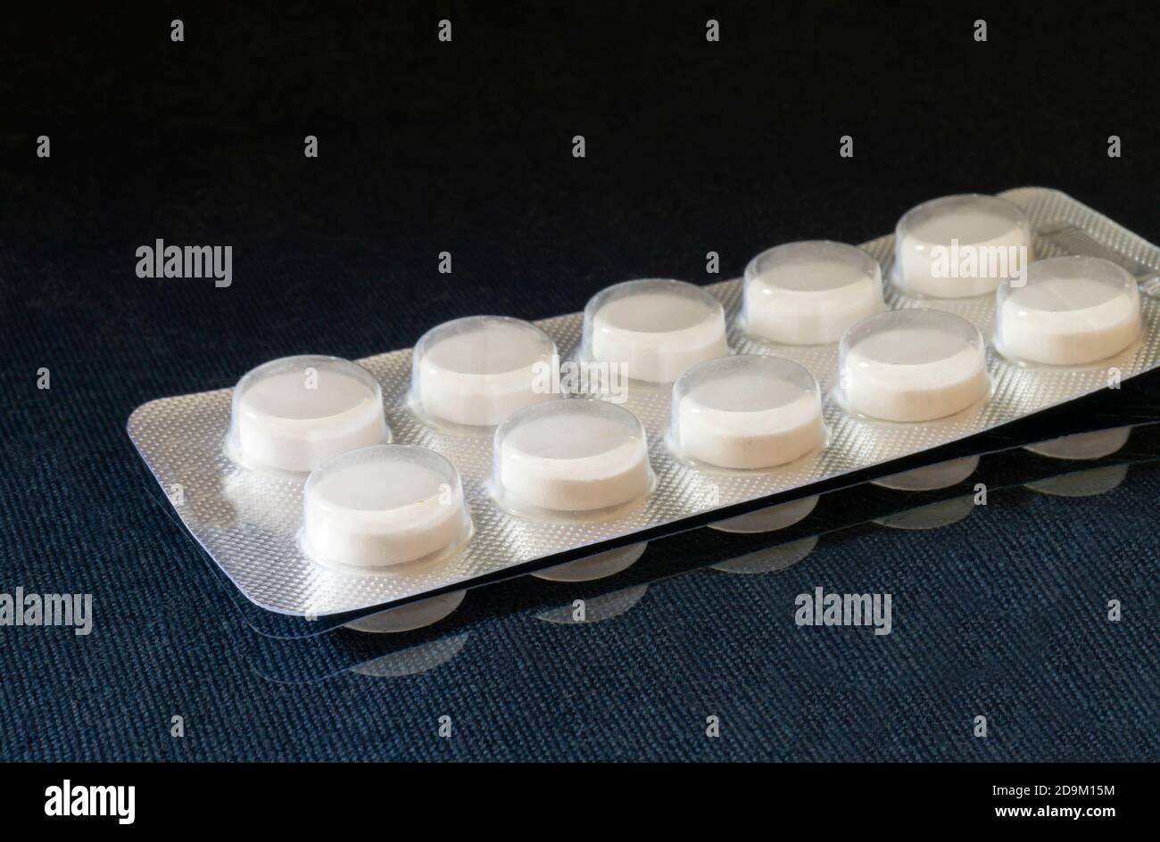 Die medizinischen Pillen in der Verpackung auf schwarzem Hintergrund. Verpackung mit Tablet auf Tisch mit Reflexion Stockfoto