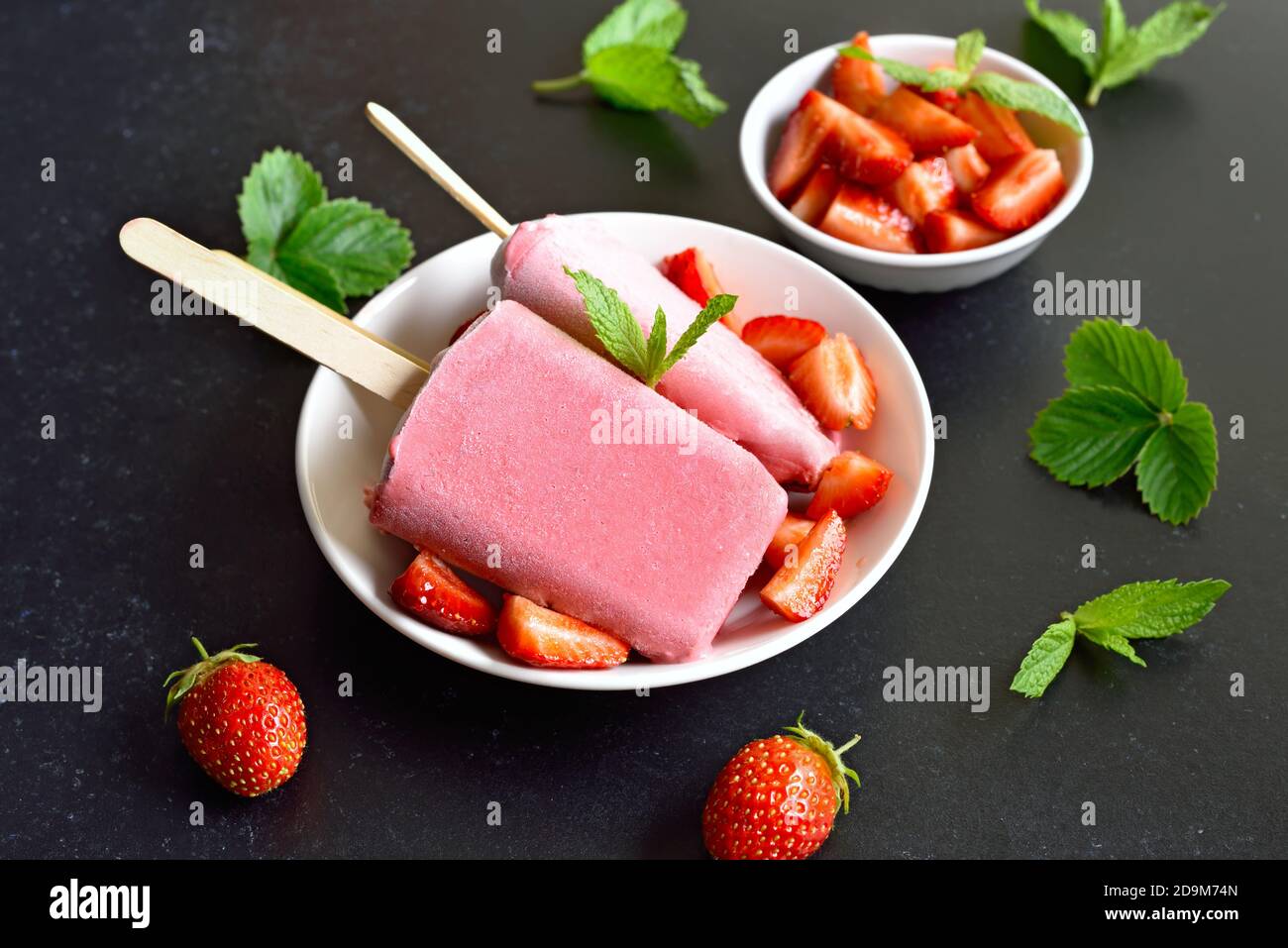 Erdbeer-Eis-Eiszapfen auf weißem Teller auf dunklem Steingrund. Stockfoto