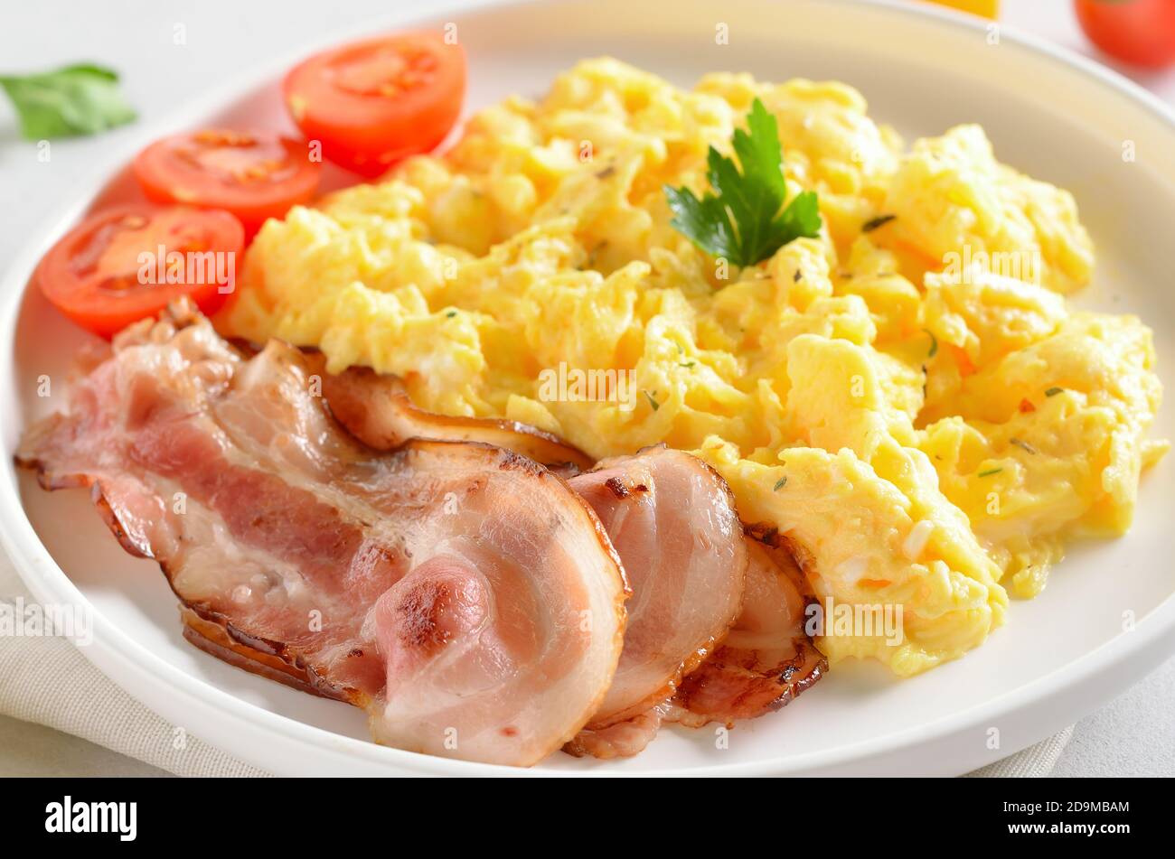 Rührei, gebratener Speck und Tomaten auf weißem Teller, Nahaufnahme Stockfoto