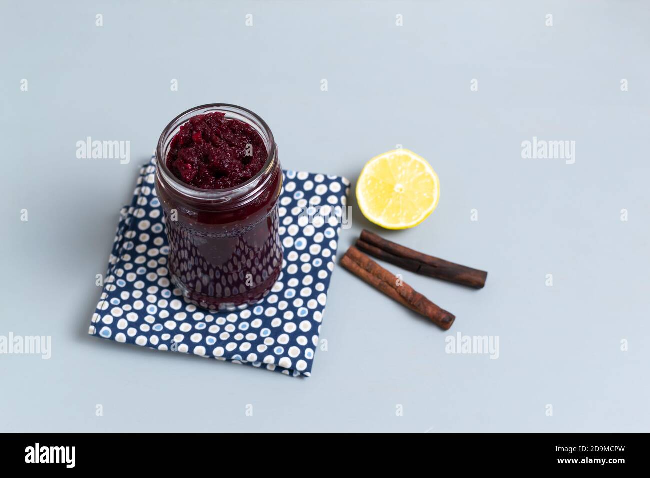 Natürliche Rübenkonfitüre in einem Glas mit Zitrone und Zimt auf einer blauen Serviette auf grauem Hintergrund. Vegetarismus-Konzept. Speicherplatz kopieren. Selektiver Fokus. Stockfoto