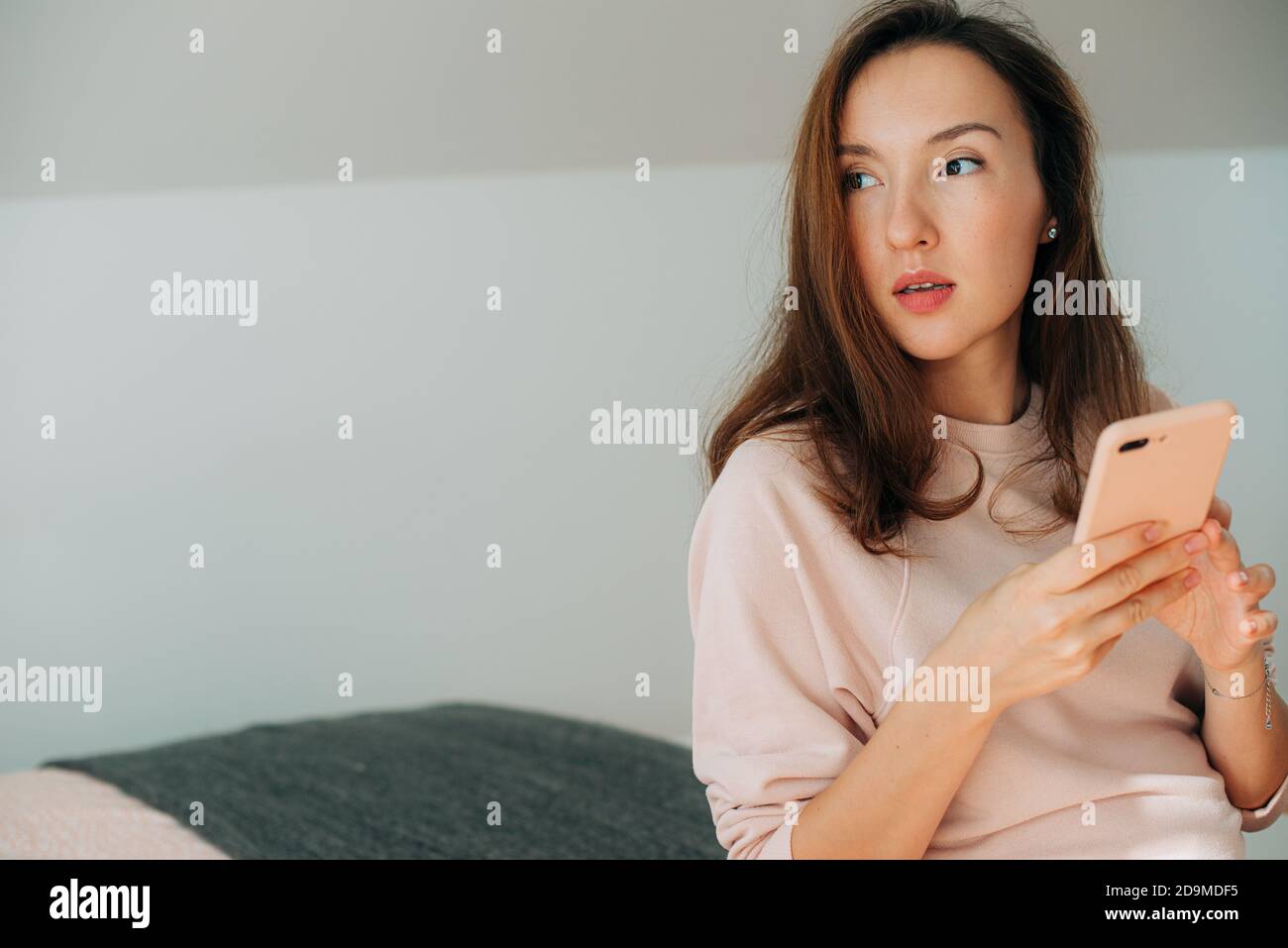 Asiatische Frau hält Smartphone während sitzen und beiseite schauen Stockfoto