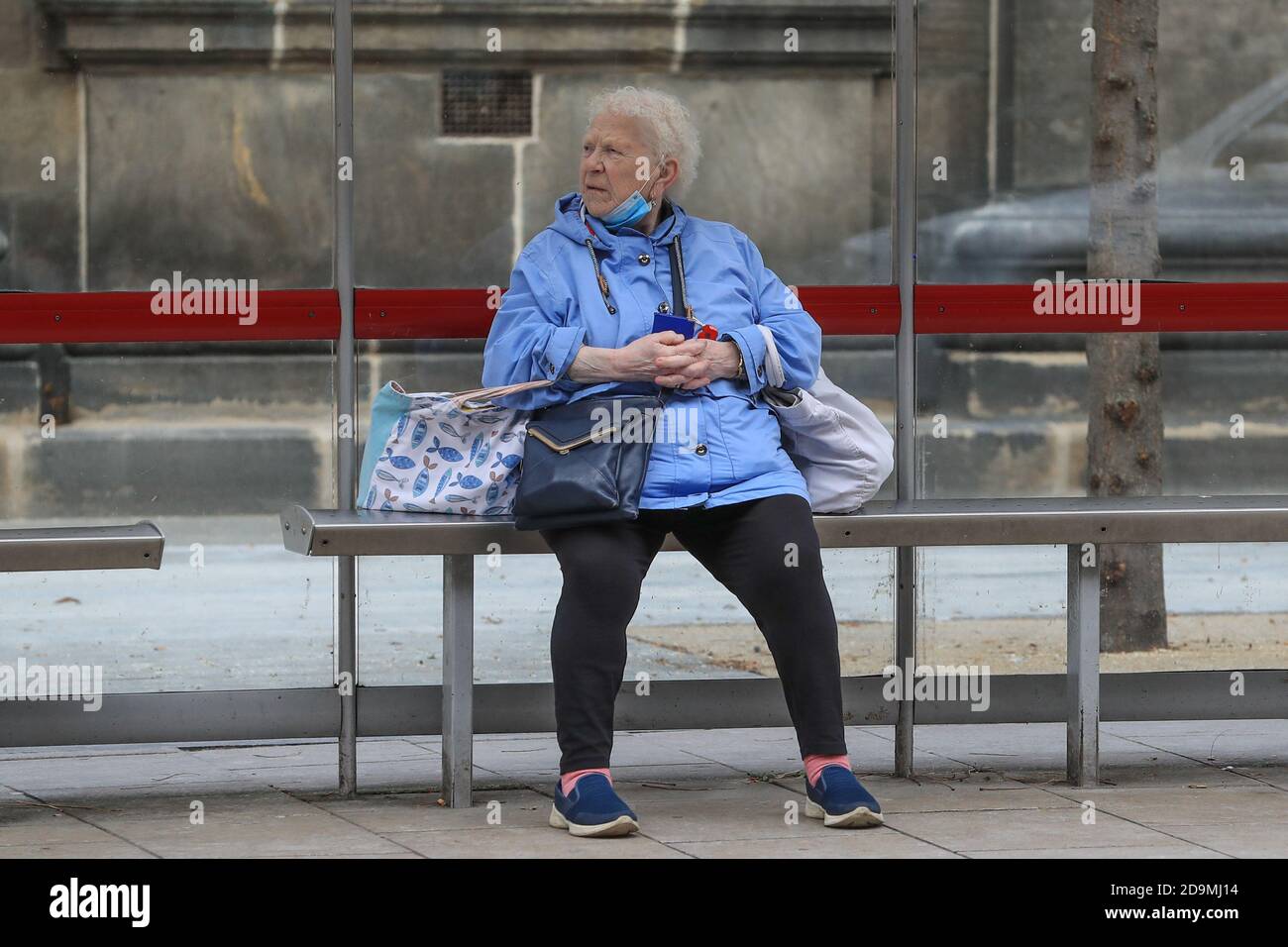 Eine Dame wartete mit ihr auf ihren Bus nach Hause Maske hing unter ihrem Kinn während Covid-19 Tag eins Lockdown 2 auf den Straßen von Leeds City Centre Stockfoto