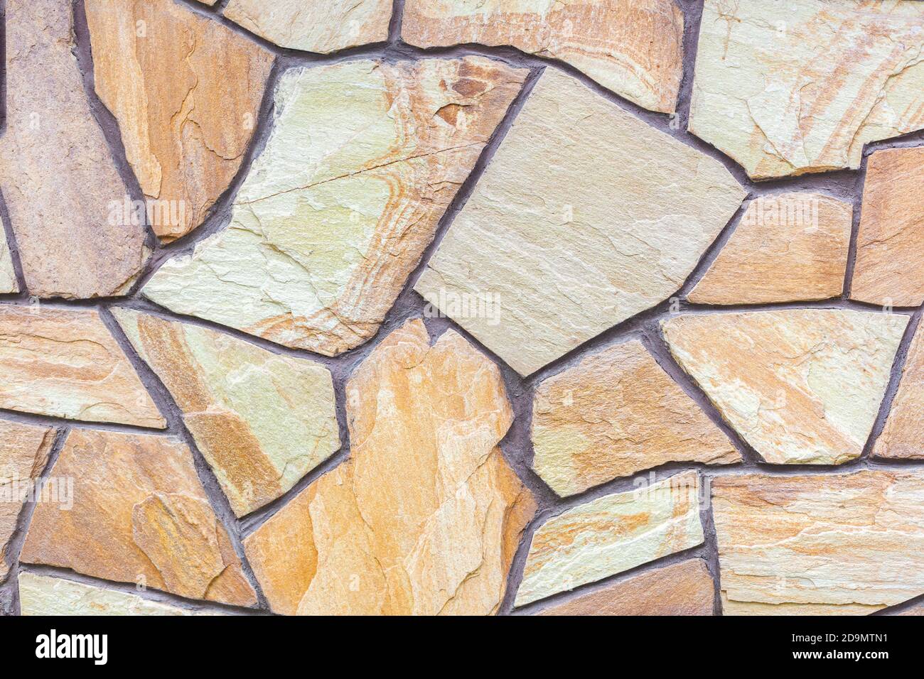 Nahaufnahme einer mit Sandsteinfliesen gefliesten Wand. Design, Konstruktion. Chaotisches Steinmosaik. Naturstein. Ein vielseitiger Hintergrund für verschiedene Zwecke Stockfoto