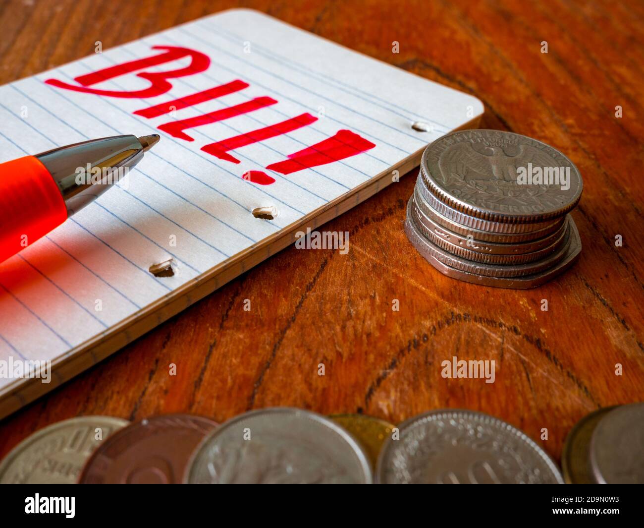 Münzbestand, Notizblock mit dem Wort Bill! Vor der Stiftspitze und einem Haufen Münzen im Vordergrund. Stockfoto