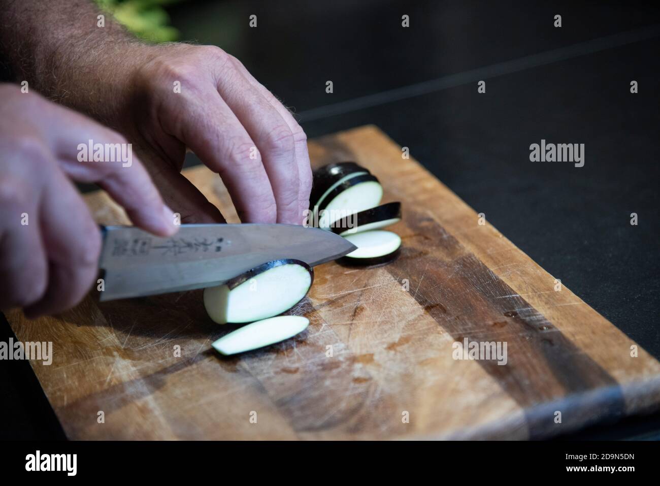 Auberginen ernten und vegetarisch kochen: Gesunde und nachhaltige Ernährung aus dem eigenen Garten. Auberginen mit einem santoku-Messer schneiden. Stockfoto