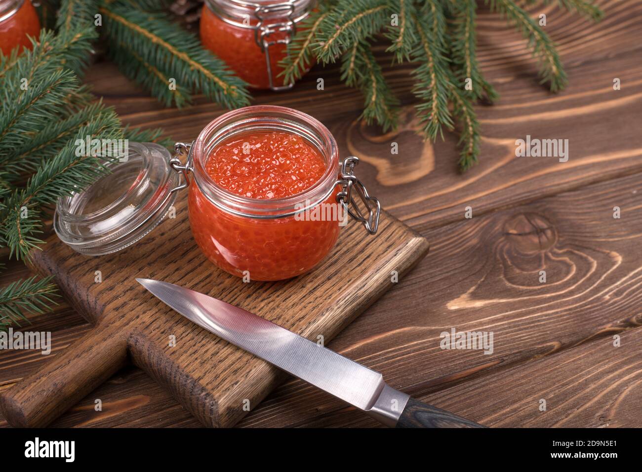 Roter Kaviar im Glas auf braunem Holzgrund mit Weihnachtsbaum. Das Hauptgericht des neuen Jahres. Stockfoto