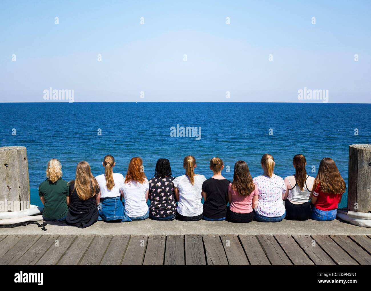 Eine Gruppe Mädchen sitzen nebeneinander auf dem Pier und blicken auf das Meer, Helgoland, Schleswig-Holstein, Deutschland Stockfoto