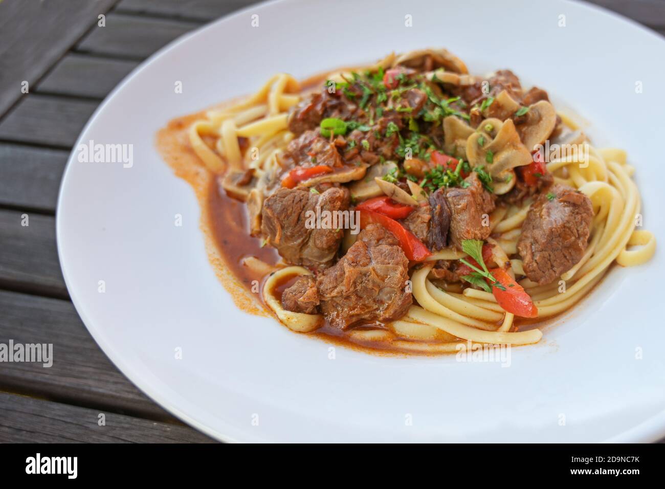 Ragout aus Rindfleisch, rote Paprika und Pilze mit Petersilie garnieren auf Pasta in einem weißen Teller auf einem dunklen rustikalen Holztisch, Kopierer Platz, ausgewählt fo Stockfoto