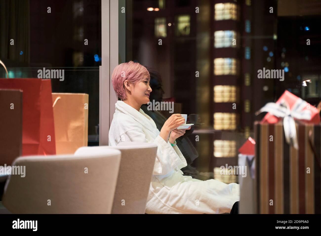 Junge asiatische Frau, die sich im Hotelzimmer entspannt und danach Kaffee trinkt einkaufen von Weihnachtsgeschenken Stockfoto