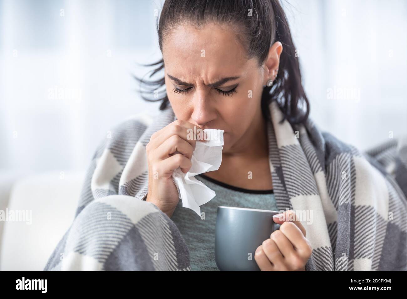 Frau mit Grippe hustet und hält eine Tasse heißen Tee. Stockfoto