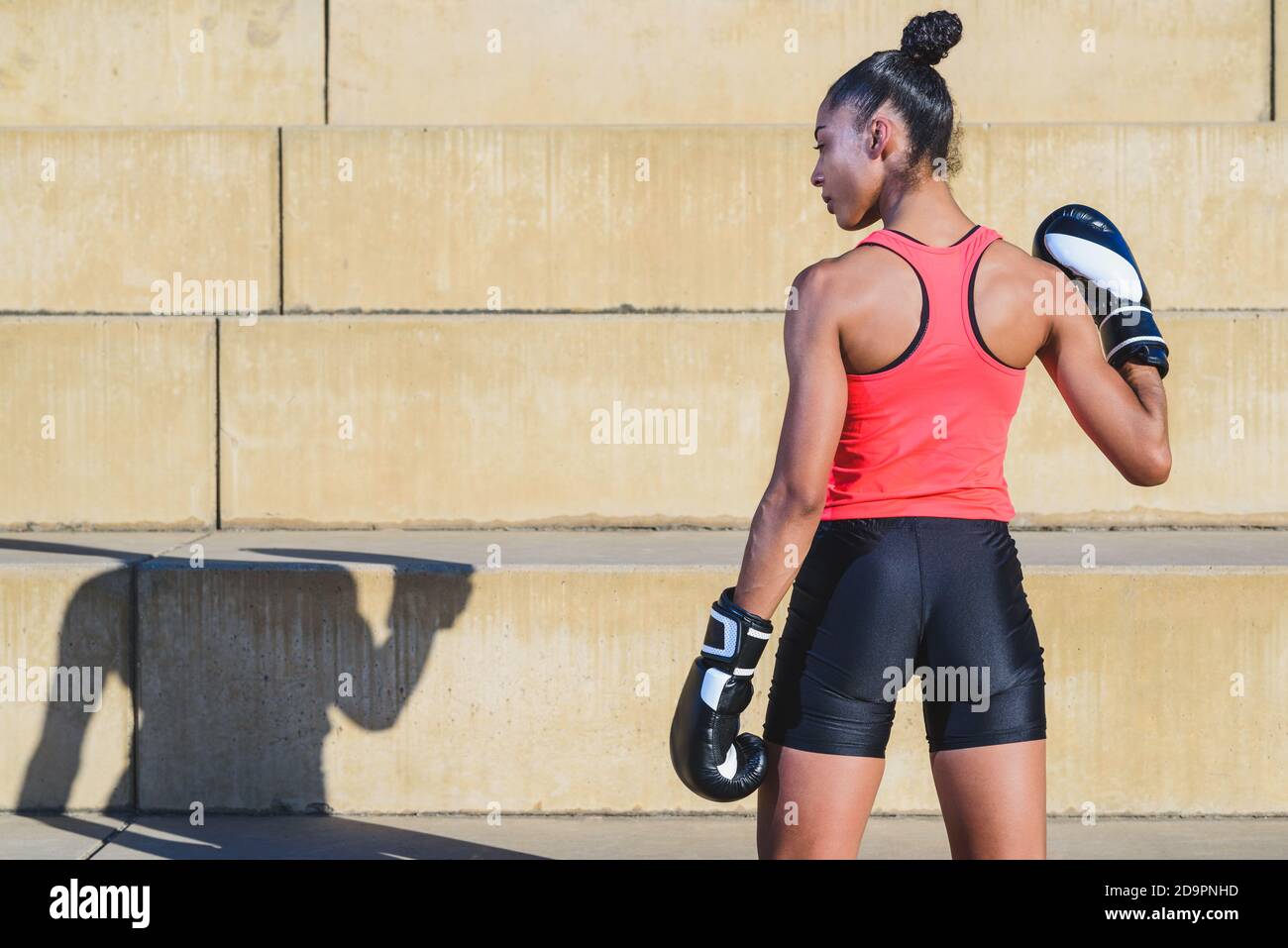 Zurück Porträt der afrikanischen Boxerin mit Haaren gebunden In einem Pferdeschwanz trägt Sportkleidung und schwarz-weiß Boxen Handschuhe in einem Outdoor-Park und Cast Stockfoto
