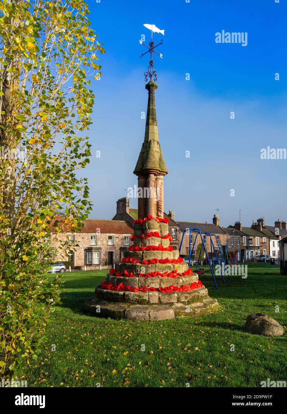 Der Markt aus dem 12. Jahrhundert kreuzt auf Norham Dorf grün in roten Mohnblumen für Remembrance Day, Norham, Northumberland, England dekoriert Stockfoto