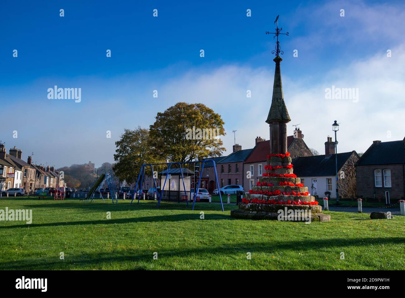 Der Markt aus dem 12. Jahrhundert kreuzt auf Norham Dorf grün in roten Mohnblumen für Remembrance Day, Norham, Northumberland, England dekoriert Stockfoto