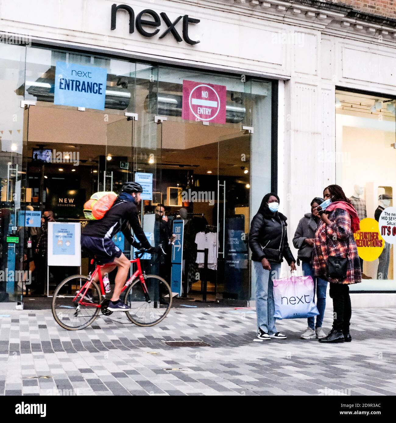 Shopper vor EINEM Next High Street Fashion Shop während der COVID-19 Coronavirus Trägt Schützende Gesichtsbedeckungen Stockfoto