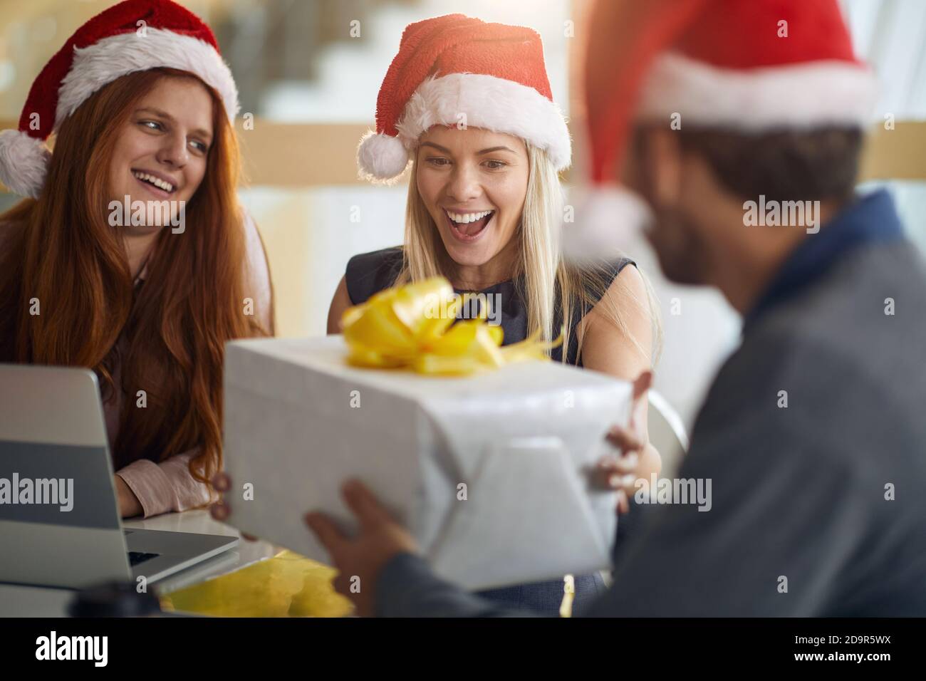 Angenehm überrascht kaukasischen weiblichen Kollegen unter eingewickelten Geschenk für weihnachten Weihnachtsmütze tragen Stockfoto