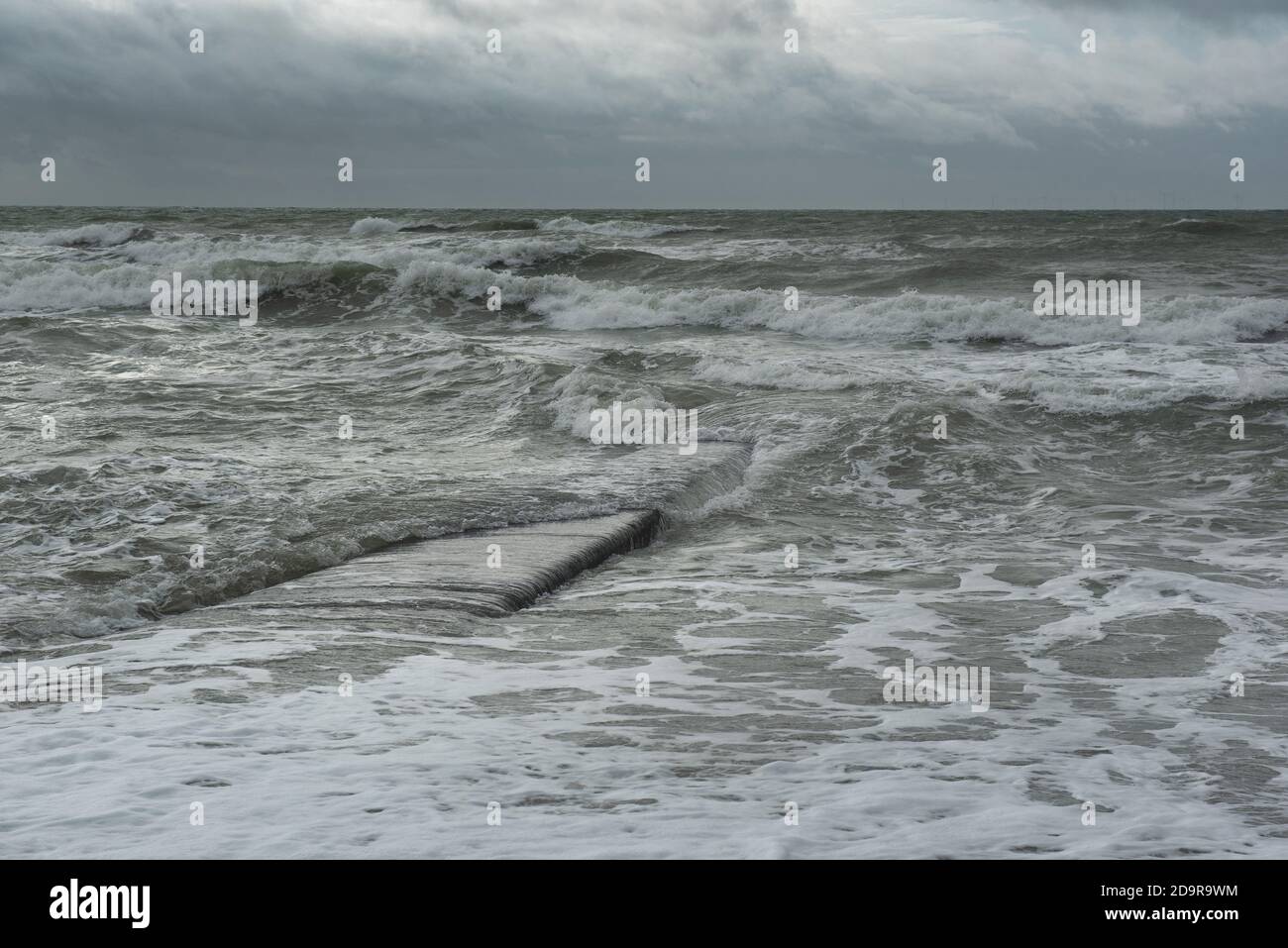 Eine Meereswelle bedeckt eine Betongroyne. Stromy Wetter in Brighton Stockfoto