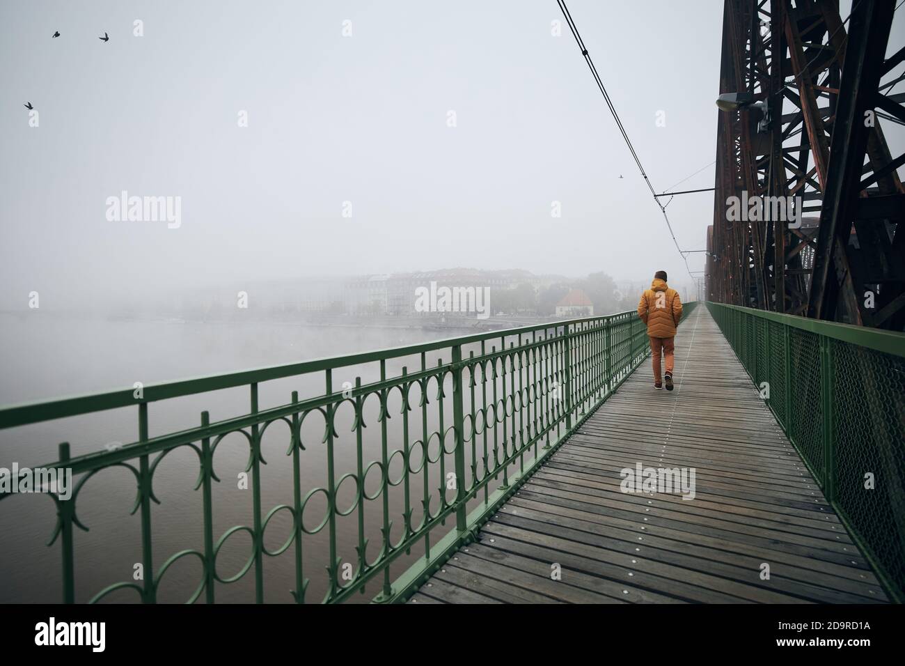 Einsamer Mann, der auf der Brücke gegen die Stadt im geheimnisvollen Nebel geht. Düsteres Wetter in Prag, Tschechische Republik. Stockfoto