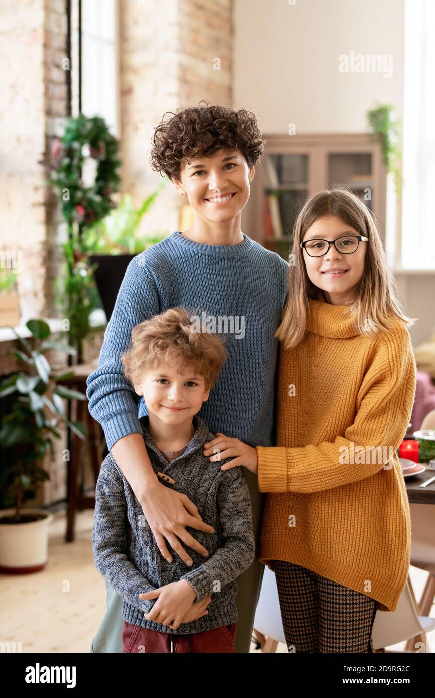 Junge fröhlich Brünette Frau in Casualwear umarmt ihre beiden niedlich Kinder Stockfoto