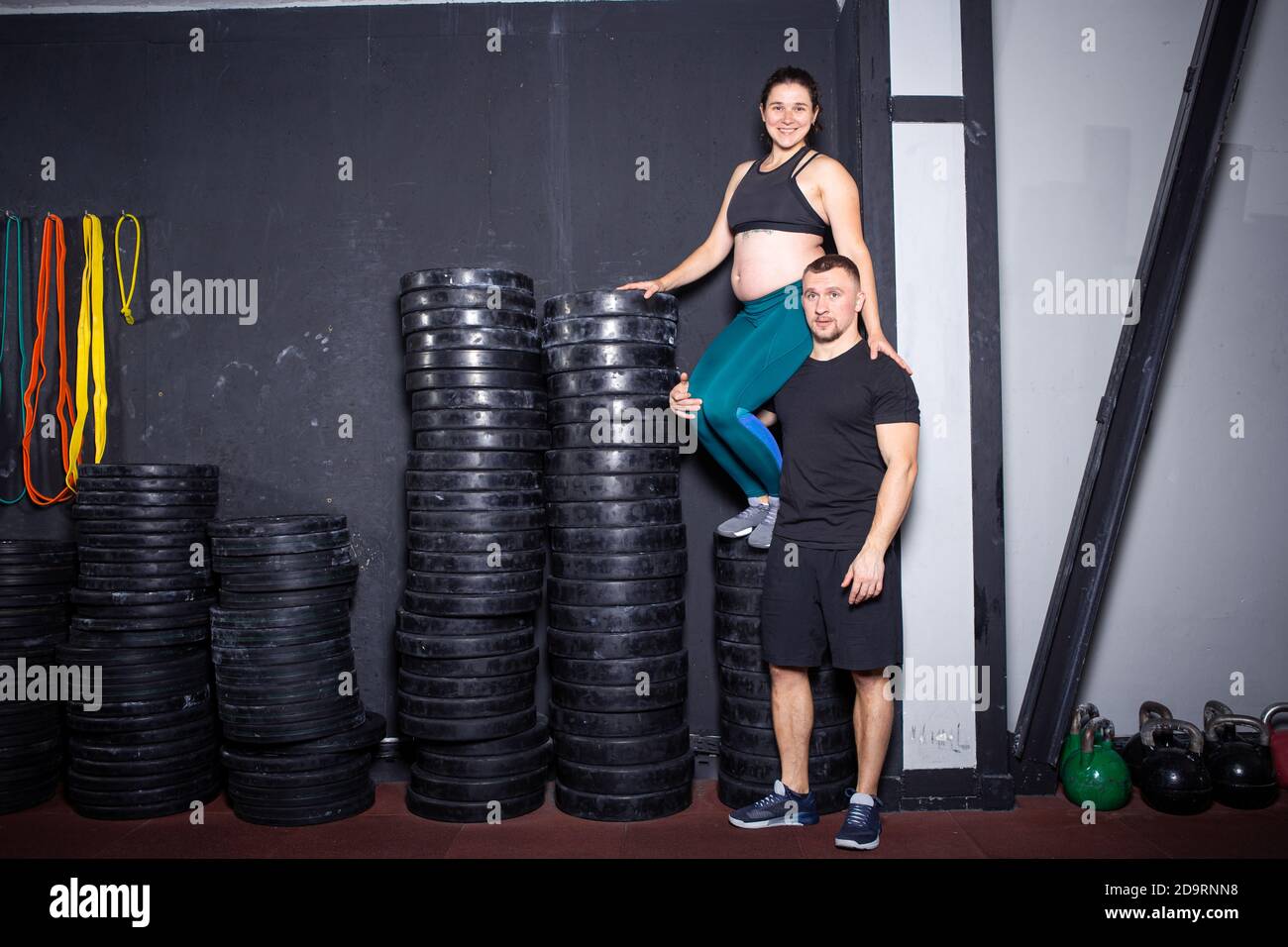 Workouts und Übungen für schwangere Frauen im Fitnessstudio. Kaukasische Athleten Bodybuilder, Ehepaar Ehemann und Ehefrau genießen Schwangerschaft und posieren nach Stockfoto