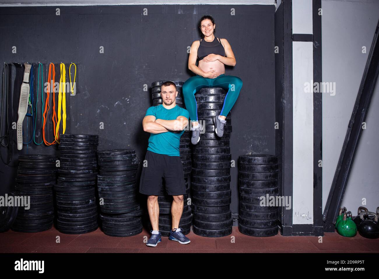 Workouts und Übungen für schwangere Frauen im Fitnessstudio. Kaukasische Athleten Bodybuilder, Ehepaar Ehemann und Ehefrau genießen Schwangerschaft und posieren nach Stockfoto