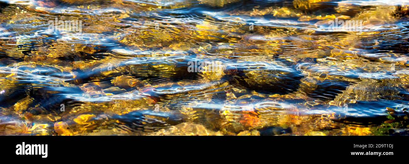 Ein abstraktes Bild, das vom Wind erzeugt wird, der Wellen auf der Oberfläche eines Steinpools am Strand verursacht, die Felsen unter dem Wasser, die von einem niedrigen warmen Sonnenlicht beleuchtet werden. Stockfoto