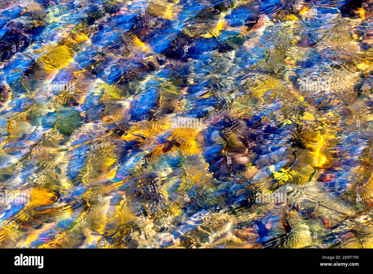 Ein abstraktes Bild, das vom Wind erzeugt wird, der Wellen auf der Oberfläche eines Steinpools am Strand verursacht, die Felsen unter dem Wasser, die von einem niedrigen warmen Sonnenlicht beleuchtet werden. Stockfoto