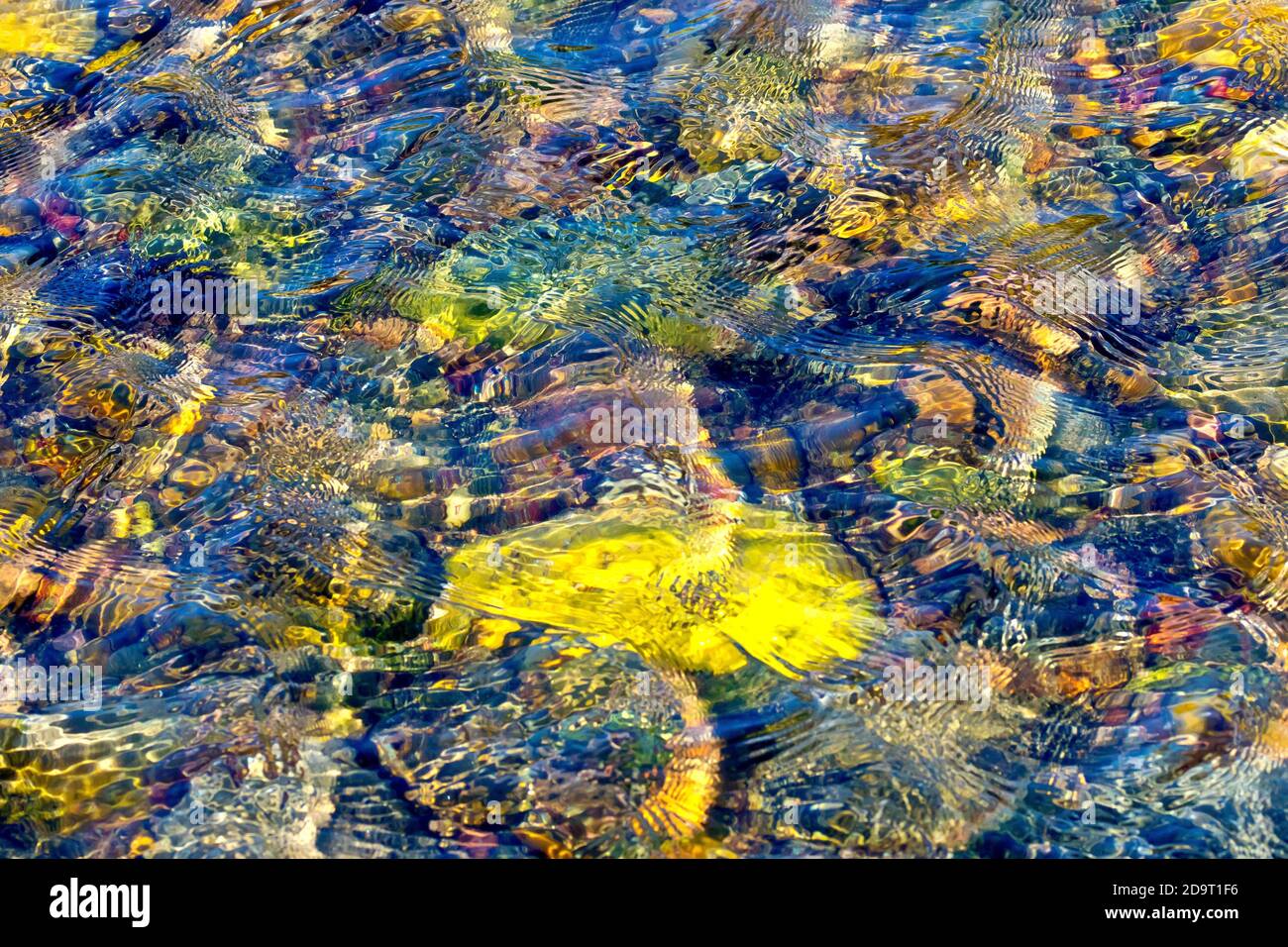 Ein abstraktes Bild, das vom Wind erzeugt wird, der Wellen auf der Oberfläche eines Steinpools am Strand verursacht, die Felsen unter dem Wasser, die von einem niedrigen warmen Sonnenlicht beleuchtet werden. Stockfoto