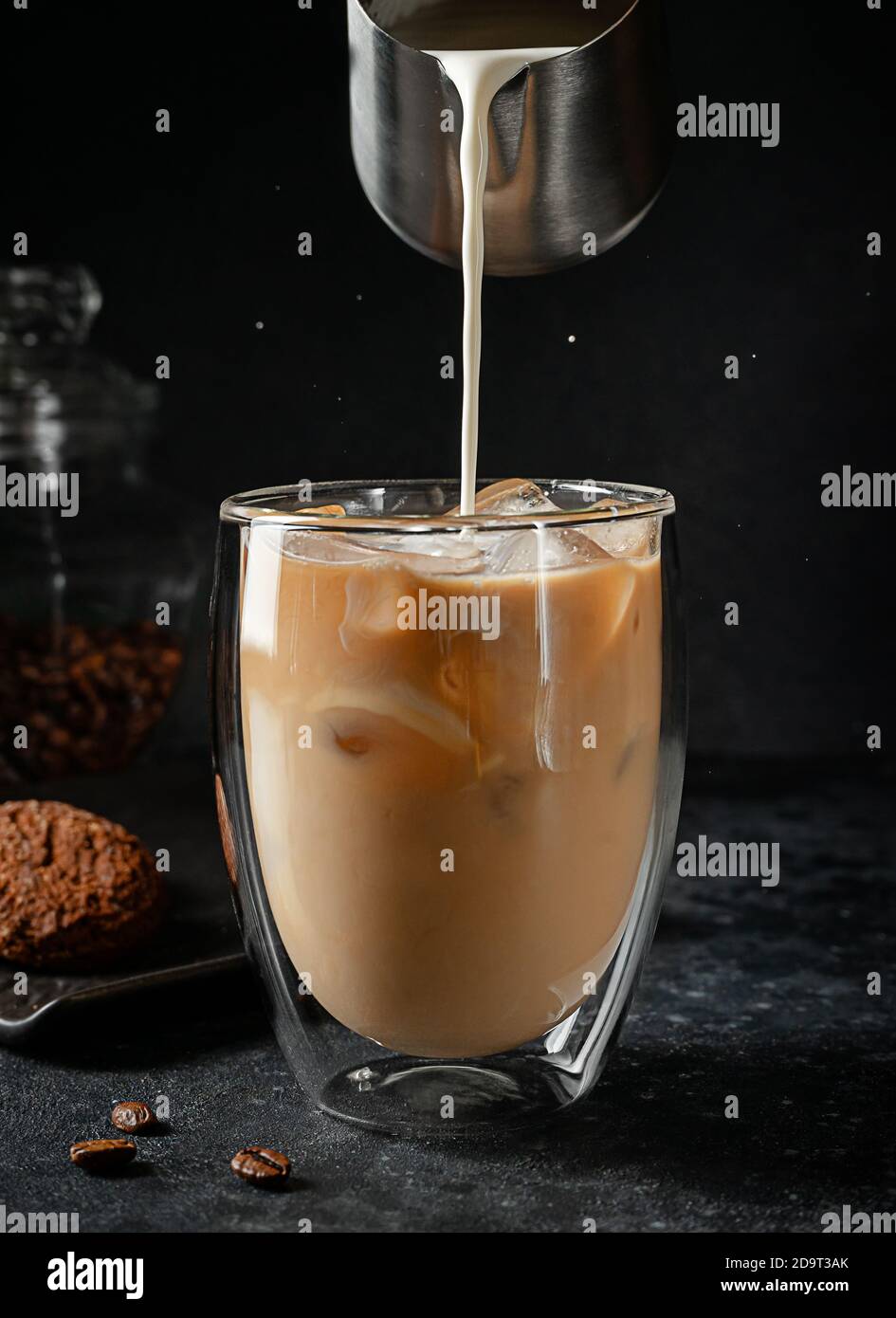 Gießen von Sahne in das Glas von Eiskaffee auf schwarzem Hintergrund. Stockfoto