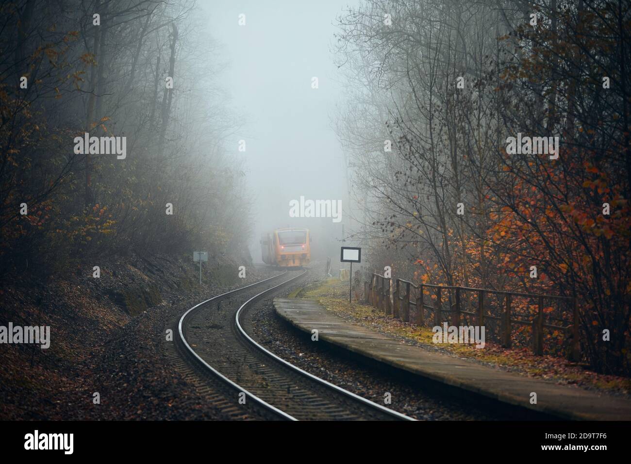 Eisenbahn bei Herbstwetter. Personenzug verlässt Bahnhof in Nebelwald. Stockfoto