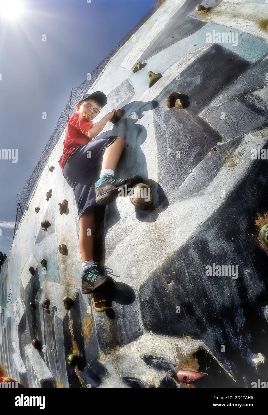 Junge klettert eine blaue Kletterwand von unten gesehen Stockfoto