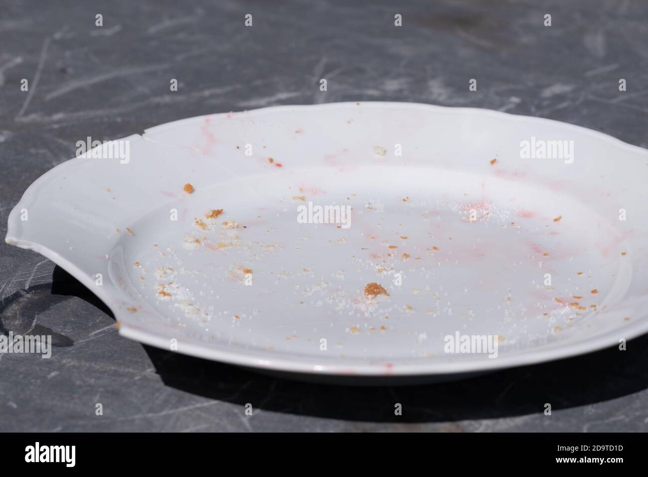 Schmutzige weiße Platte mit einem Stück weg verwendet. Krümel und Zuckergranulat sind darauf Stockfoto