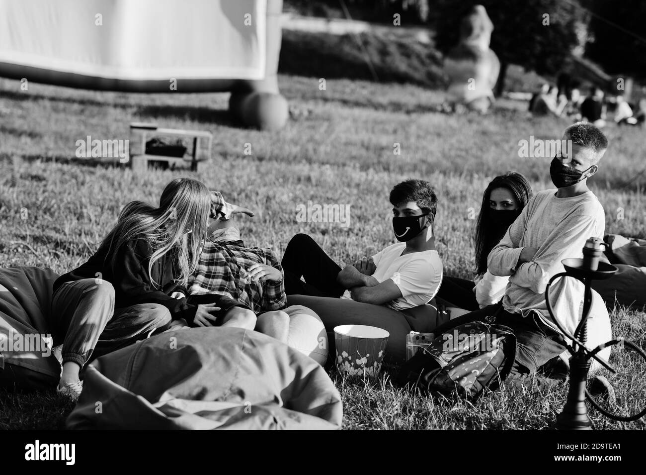 Junge multi ethnische Gruppe von Menschen, die Film an poof im Open-Air-Kino zu tragen Maske während covid Coronavirus Quarantäne. Stockfoto