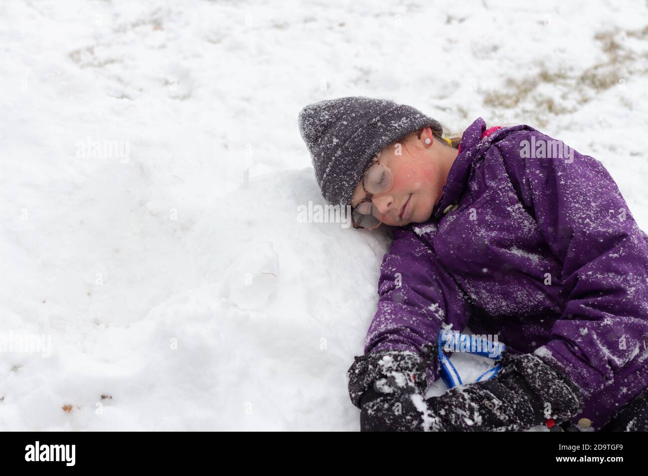 Kind, das sich im Schnee ausruhen kann, genießt es, während des Schneefalls draußen zu sein Stockfoto