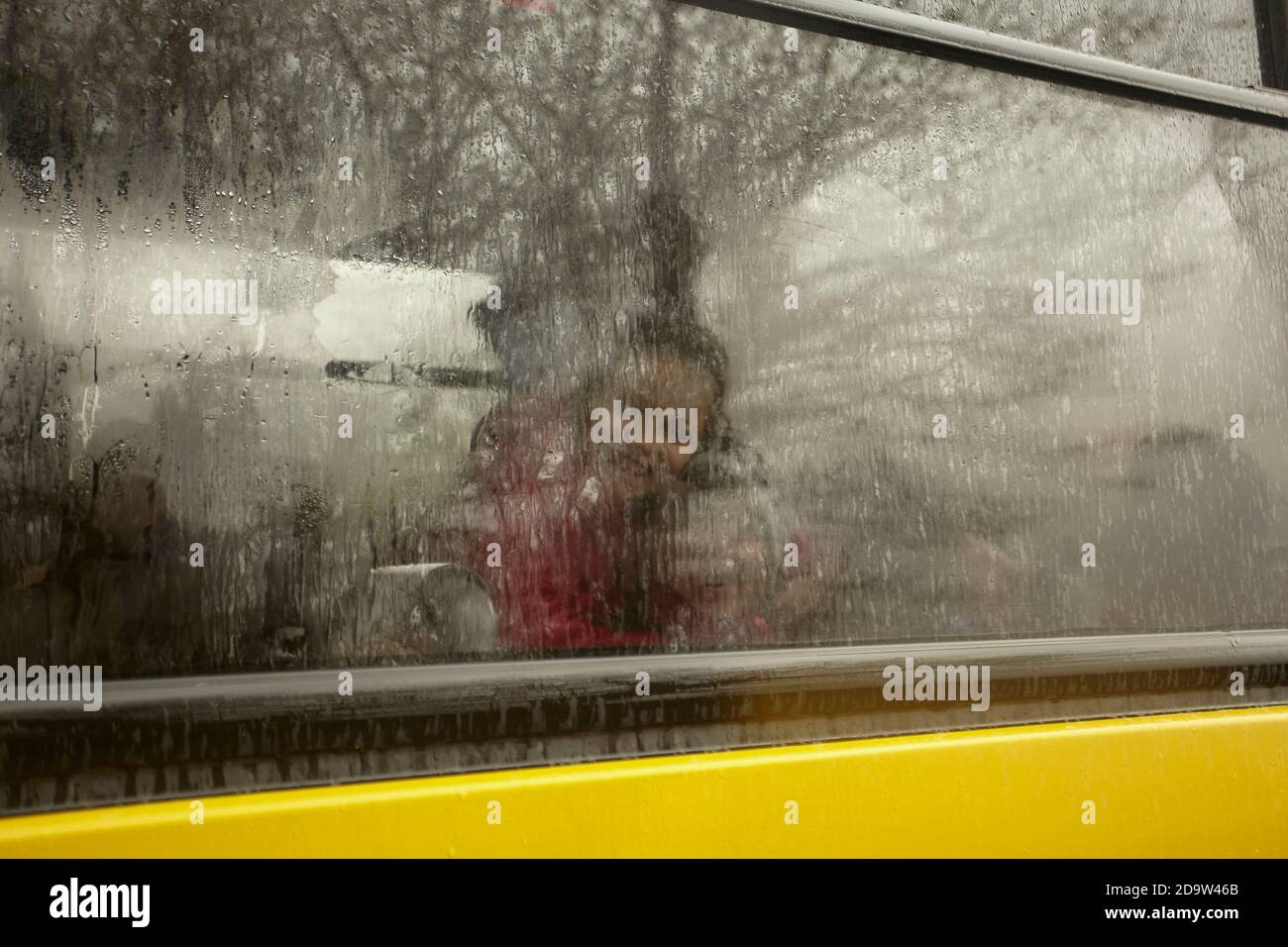 Gesichter von Kindern verschwommen und versteckt hinter einem Glas von Regen bedeckt, der unaufhörlich abfällt. Stockfoto