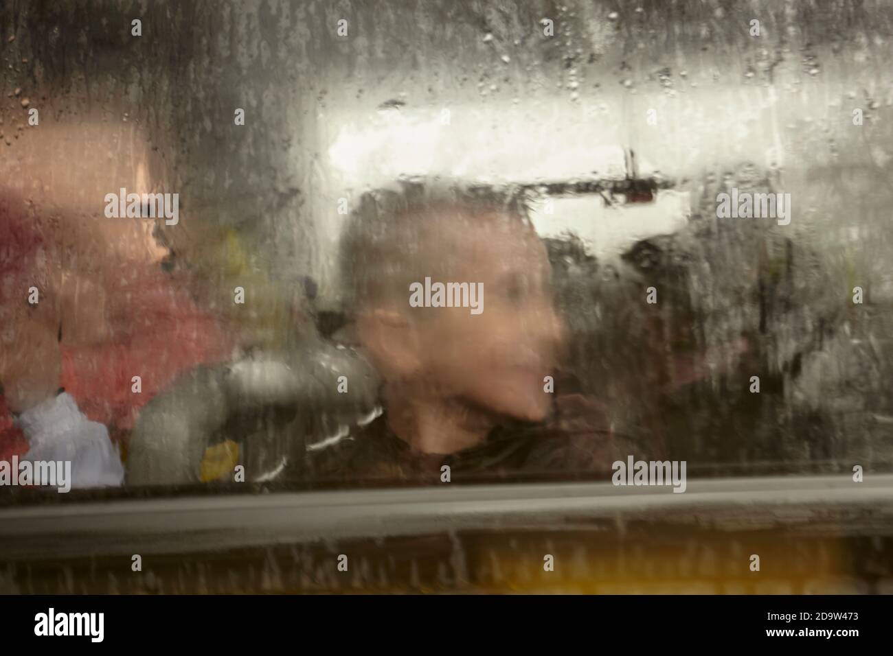 Gesichter von Kindern verschwommen und versteckt hinter einem Glas von Regen bedeckt, der unaufhörlich abfällt. Stockfoto