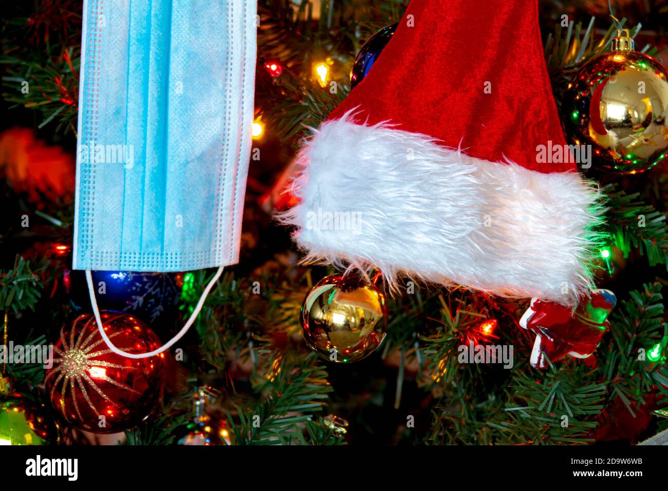 Nahaufnahme einer medizinischen Gesichtsmaske und einem Weihnachtsmann-Hut, der an einem Weihnachtsbaum hängt. Konzept: Pandemie, covid -19, Coronavirus während der Weihnachtsfeiertage Stockfoto