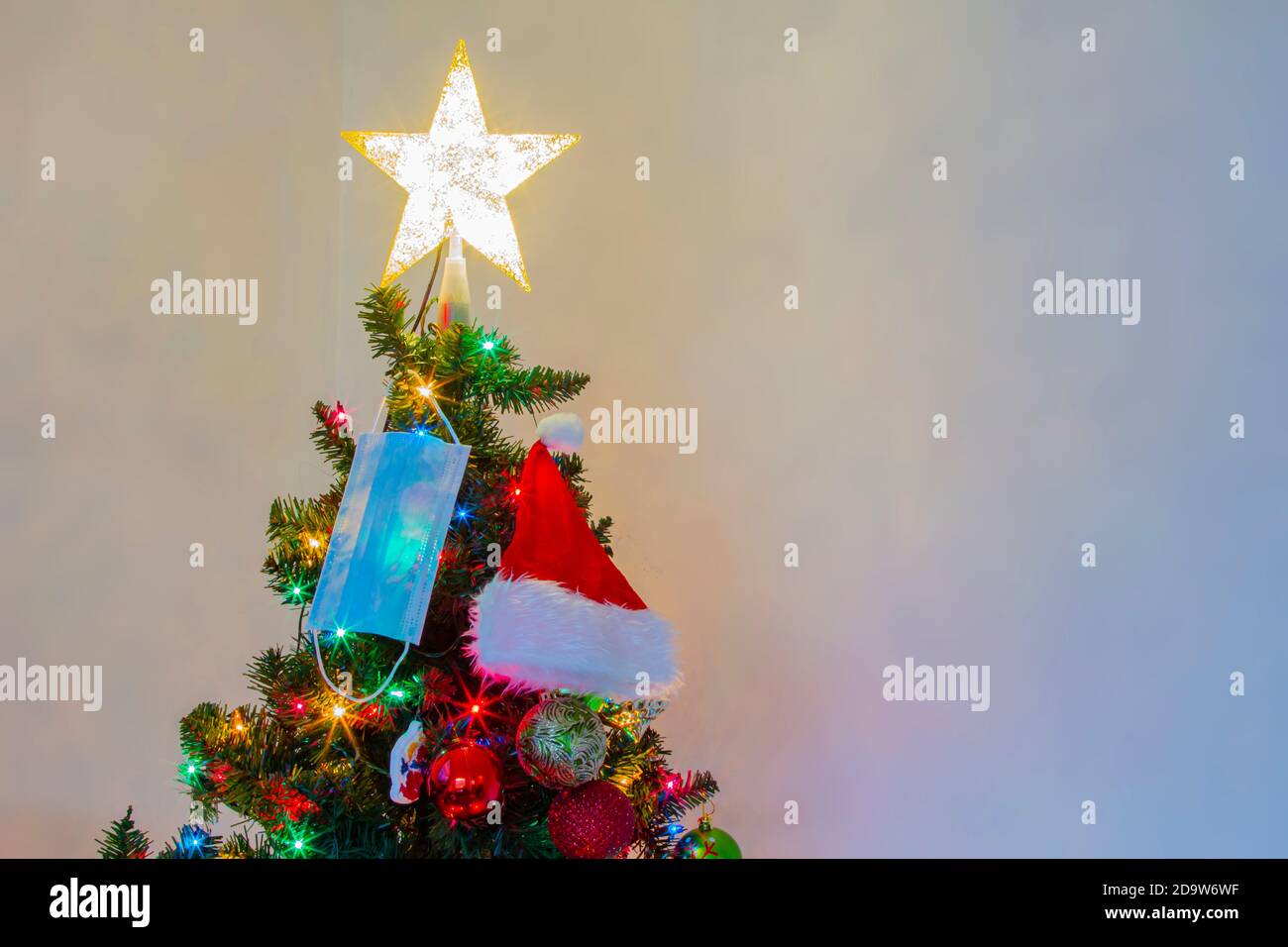 Horizontale Ansicht einer medizinischen Gesichtsmaske und eines Weihnachtsmannes, der an einem Weihnachtsbaum hängt. Konzept: Pandemie, covid -19, Coronavirus während der Weihnachtsfeiertage Stockfoto