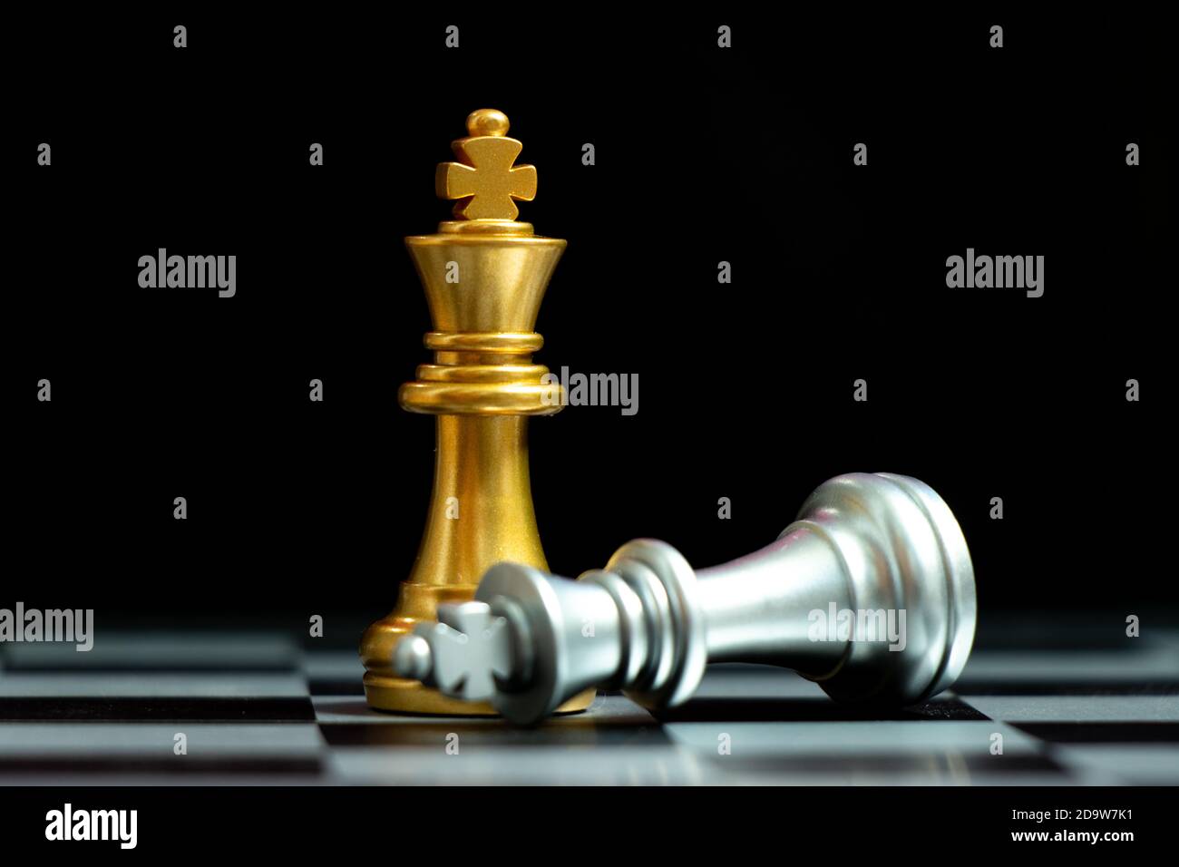Goldkönig Schachfigur gewinnen über liegend silbernen König auf schwarzem Hintergrund Stockfoto