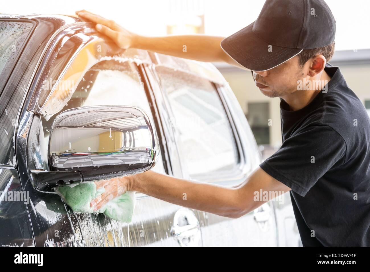 Autowascharbeiter mit T-Shirt und schwarzer Kappe reinigen das Auto in der Autowaschanlage mit einem Schwamm, Konzept für die Autopflege. Stockfoto