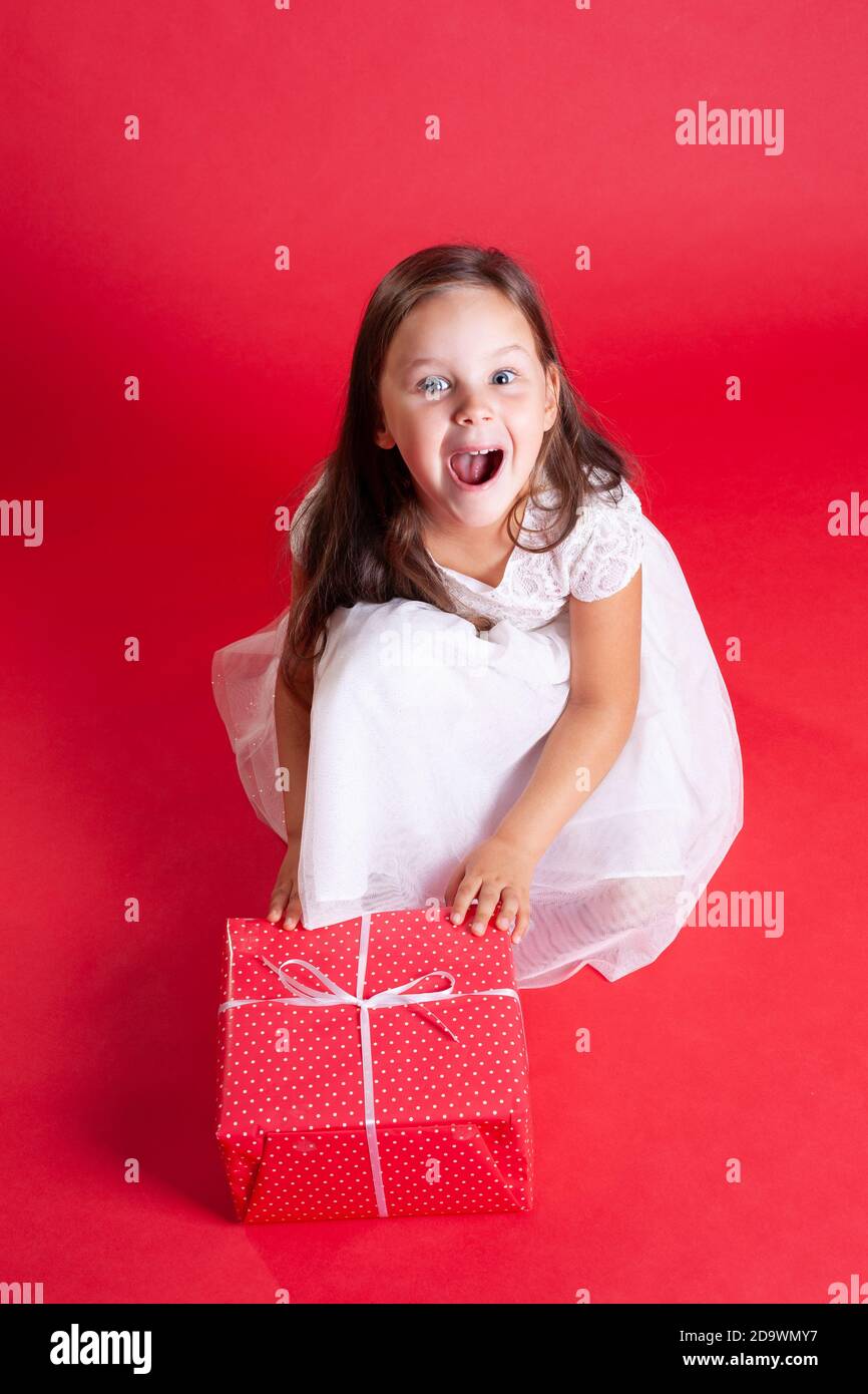 Schöne Brünette Mädchen in weiß glänzendes Kleid schreien vor Freude Beim Empfang Geschenk zu Weihnachten Mitternacht auf rotem Hintergrund Stockfoto