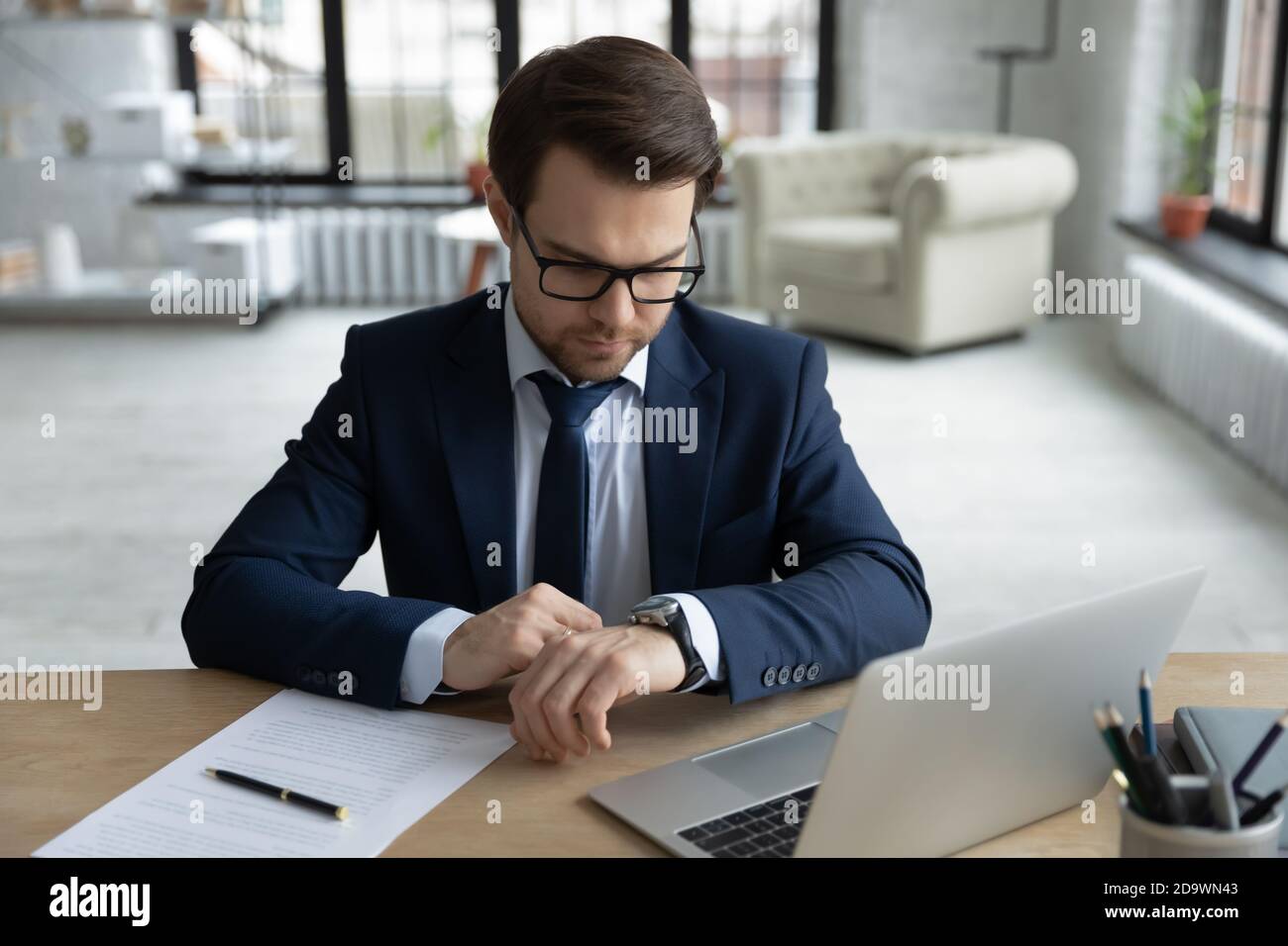 Fokussierte ernsthafte junge Geschäftsmann in Anzug Überprüfung der Zeit auf Armbanduhr. Stockfoto