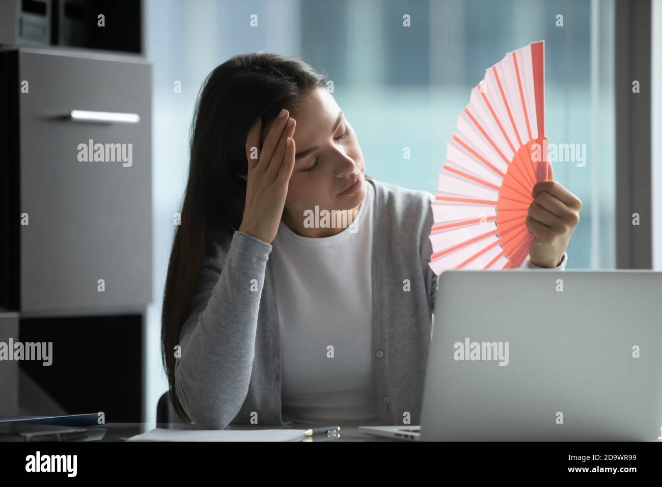 Traurige weibliche Angestellte, die wegen der Hitze im Büro die Motivation verliert Stockfoto