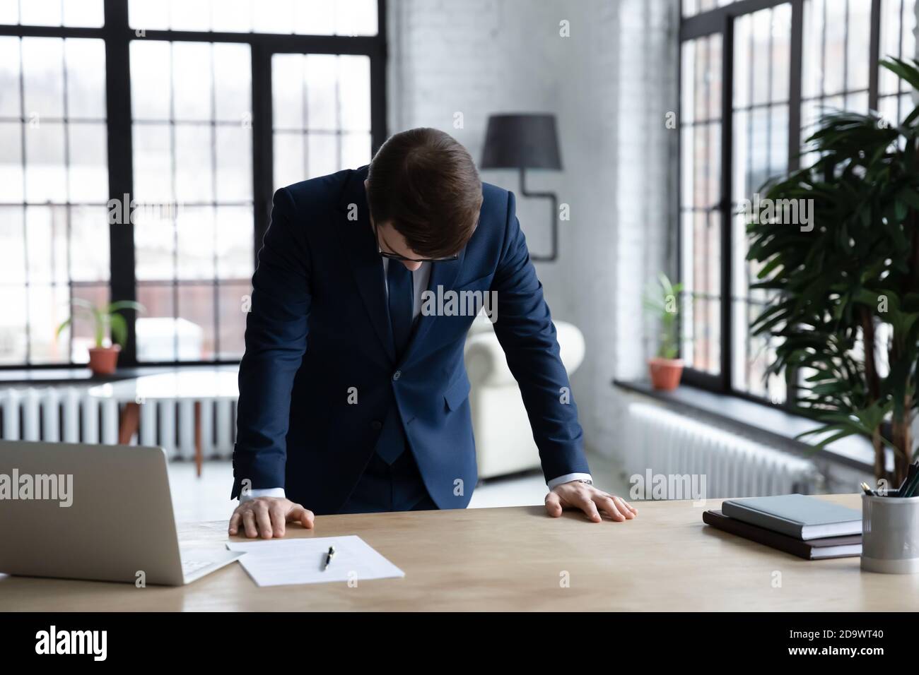 Frustrierter junger Geschäftsmann, der mit dem Kopf nach unten am Bürotisch steht. Stockfoto