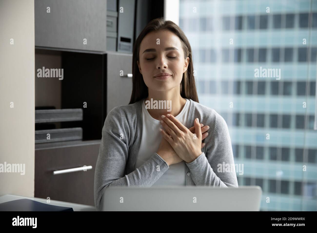 Junge Frau, die Hand an Herz legt und Gott für Hilfe dankt Stockfoto