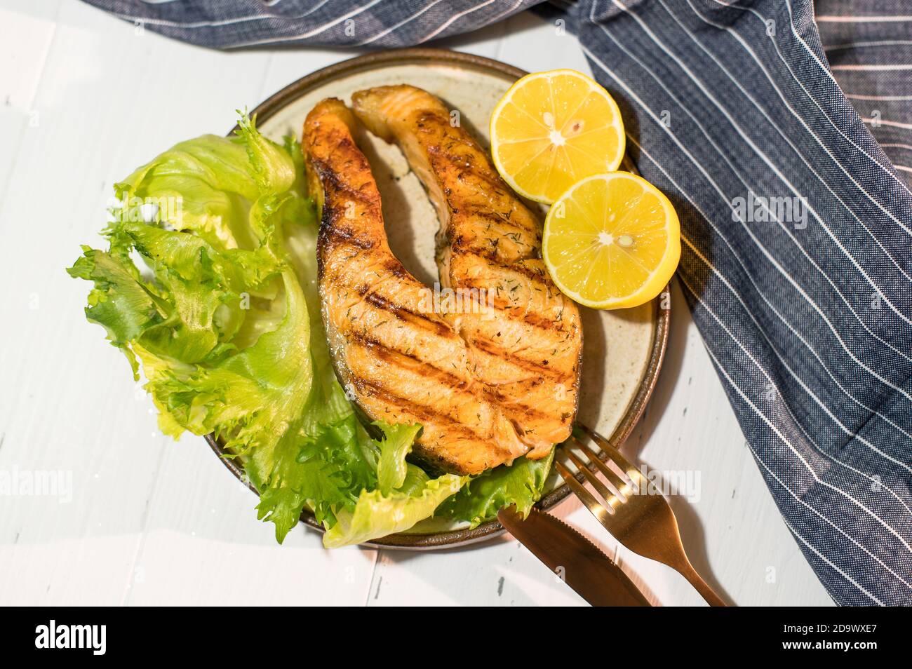 Teller gegrilltes Lachssteak mit Salat auf Holztisch mit blauer Serviette. Gegrillter frischer Fisch. Fisch für ein gesundes Abendessen Stockfoto